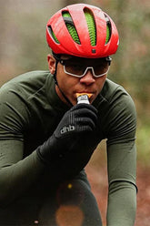Cyclist in a red helmet and gloves consuming a nutrition bar while cycling in nature.